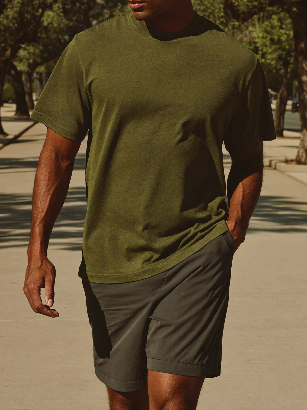 Hombre con playera oliva y short carbón caminando en una calle de concreto claro